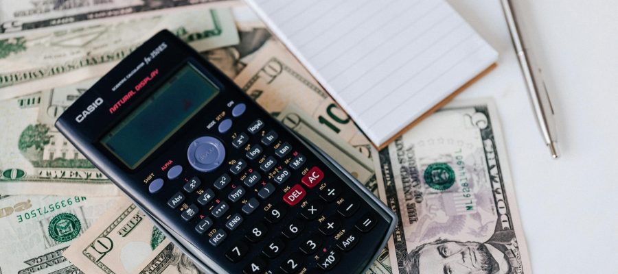 Calculator on a pile of cash with a notepad and pen, symbolizing financial organization and money mindset improvement.