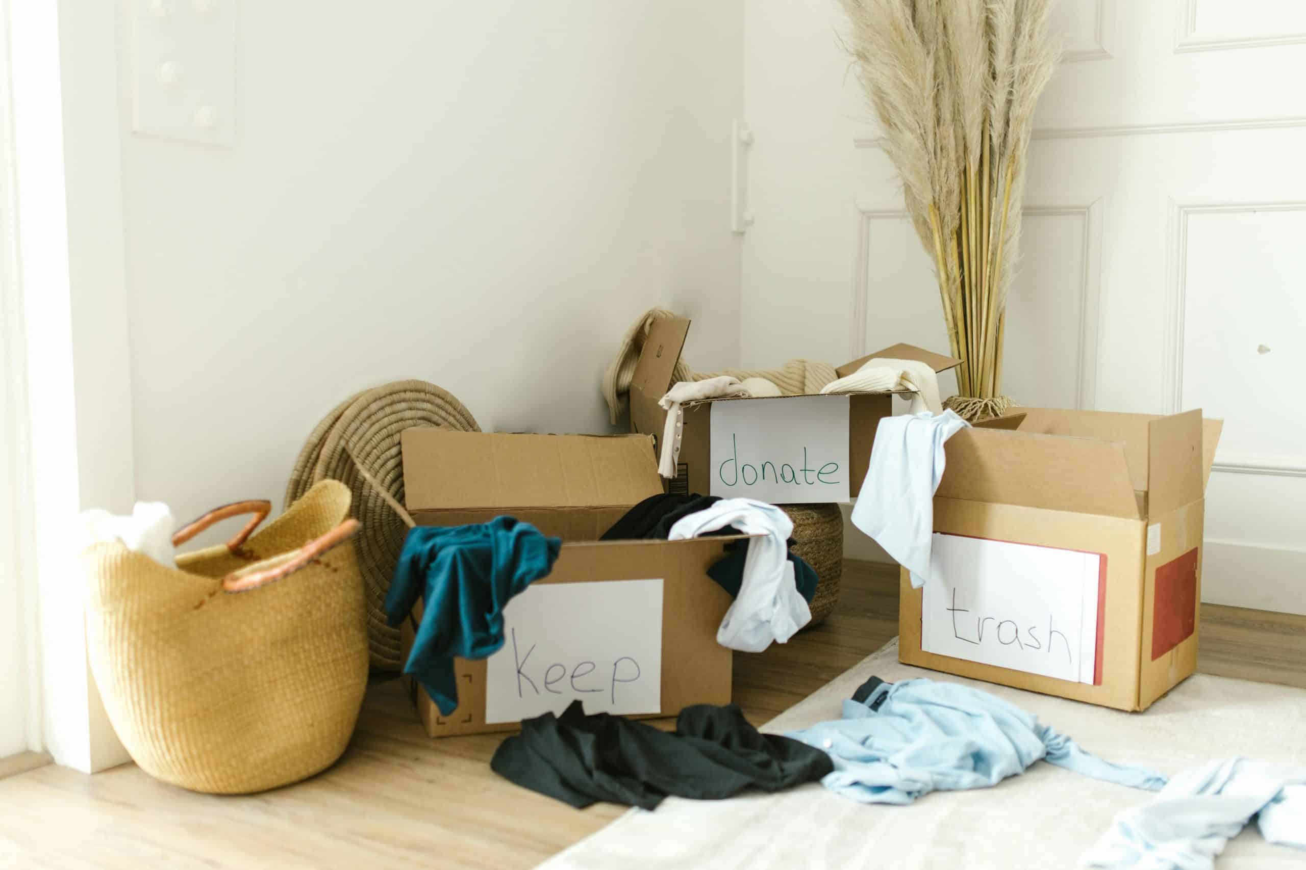 Boxes labeled "Keep," "Donate," and "Trash" filled with clothes in a bright, organized space, illustrating the process of sorting belongings for decluttering and organization.
