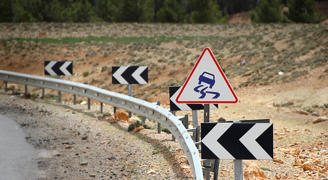 Roadside warning signs indicating a slippery road ahead, featuring a triangular caution sign with a truck icon and multiple directional arrows, emphasizing the importance of safety and awareness while driving.